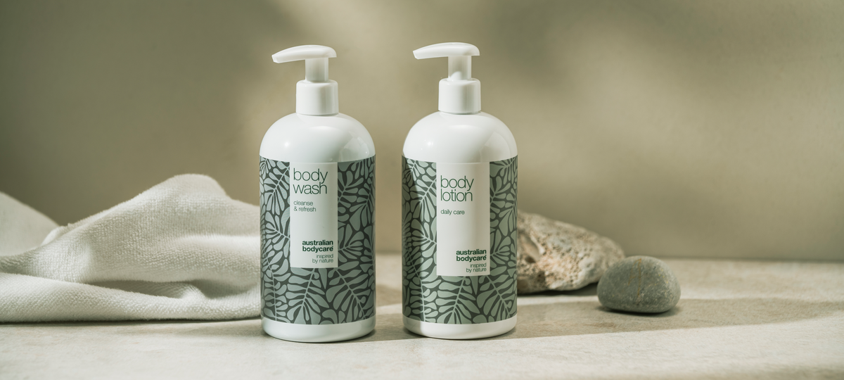 Body Wash and Body Lotion from Australian Bodycare as large pump bottles in the green tea tree design, next to a white towel and stones.