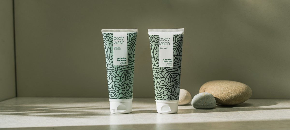Body Wash and Body Lotion from Australian Bodycare in the green tea tree design on a light stone surface, next to smooth pebbles.