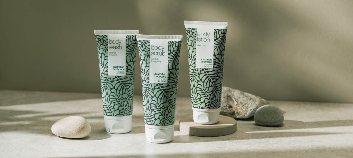 Body Wash, Body Scrub and Body Lotion from Australian Bodycare in the green tea tree design, standing on light stone plinths against an olive background.