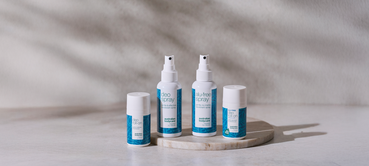 Four deodorants from Australian Bodycare on a round marble plate: Deo Roll-on, Deo Spray, Alu-free Spray and Alu-free Deo Roll-on in white and blue packaging.