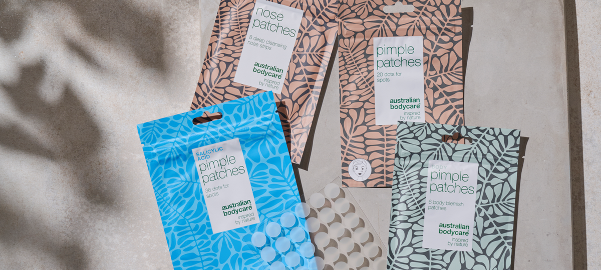 Several patch packs from Australian Bodycare layered on a stone surface: Nose Patches and Pimple Patches in beige, Salicylic Acid Pimple Patches in blue and Body Pimple Patches in green, with a sheet of patches beside them.