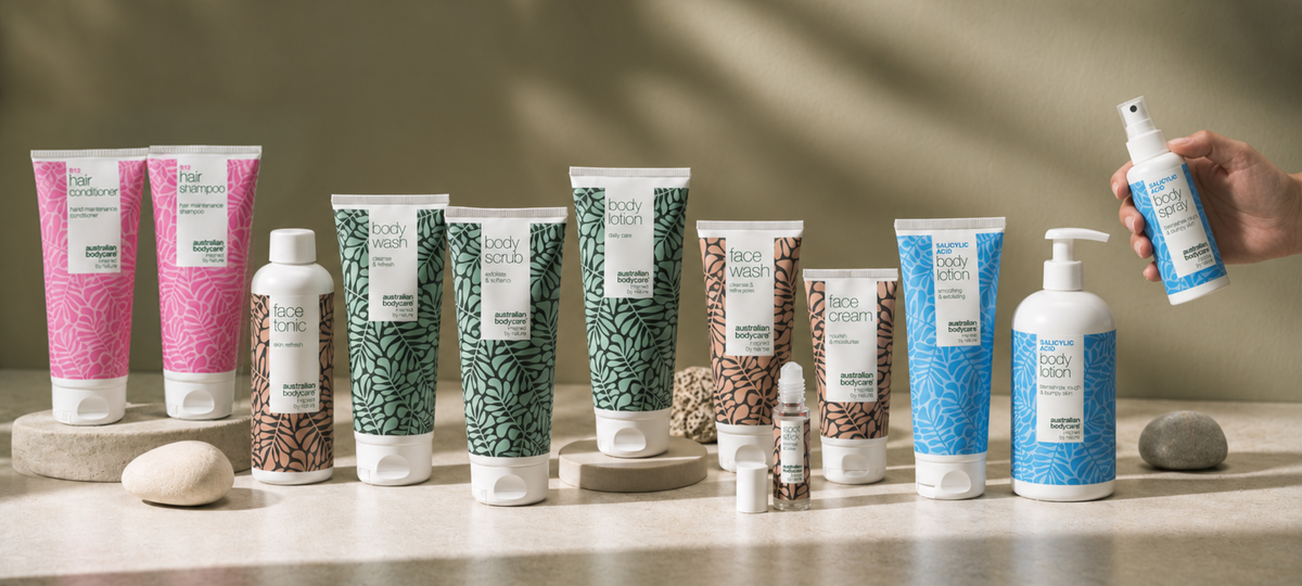 Australian Bodycare product line-up on a light stone surface: B12 Hair Shampoo and Conditioner in pink, Face Tonic, Face Wash and Face Cream in beige, Body Wash, Body Scrub and Body Lotion in green, Salicylic Acid Body Lotion and Body Spray in blue.
