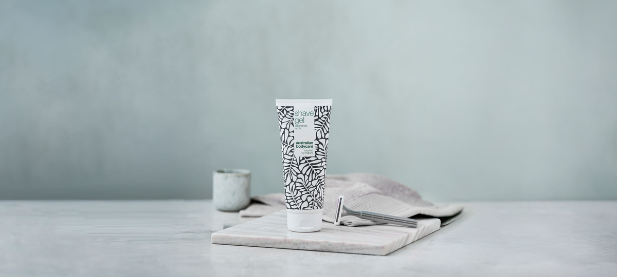 A tube of Shave Gel from Australian Bodycare in the green tea tree design on a marble board, with a safety razor and a folded towel beside it.