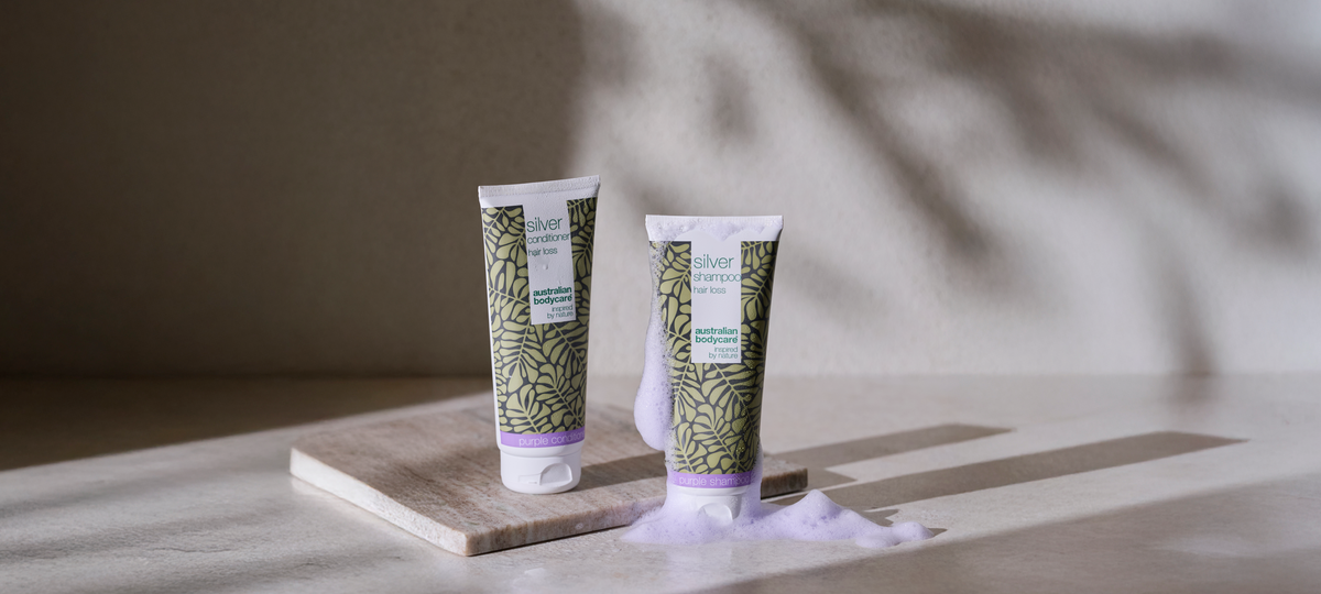 Silver Conditioner and Silver Shampoo from Australian Bodycare with purple cap rims on a marble board, next to purple-tinted foam.