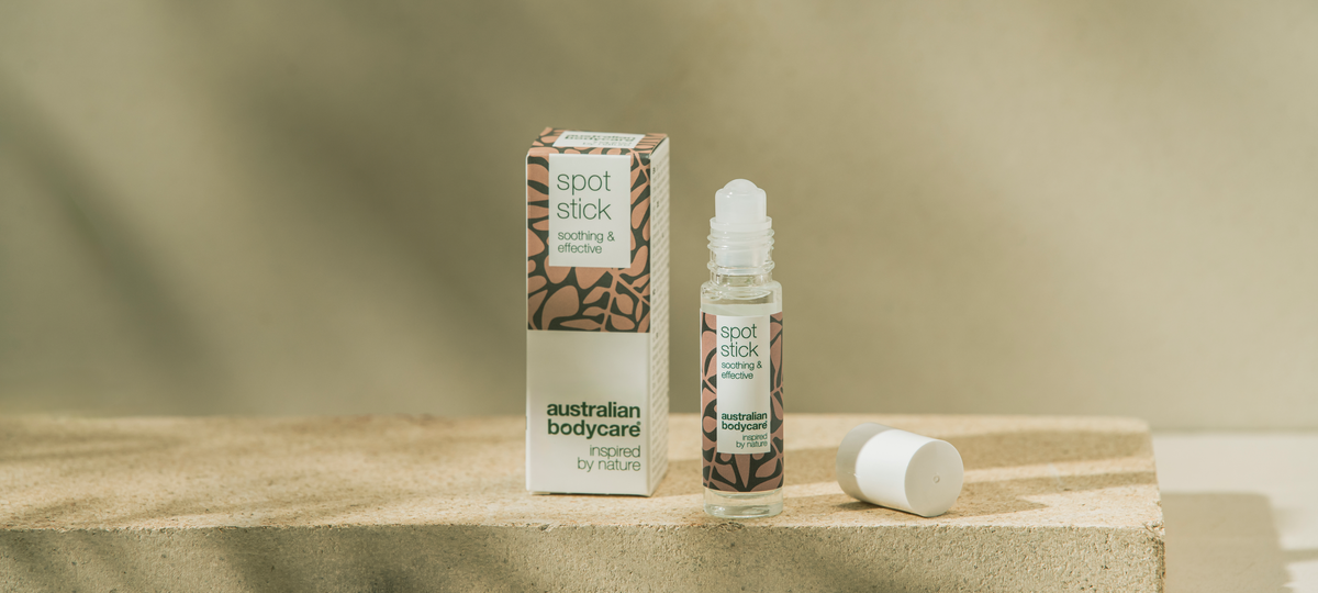 The Spot Stick roll-on from Australian Bodycare next to its beige carton on a stone block, with the cap lying beside it.