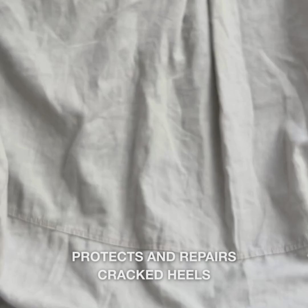 Close-up of a hand scooping a rich, creamy Heel Repair formula into the palm and gently massaging it into dry, cracked skin on the heel: the thick texture is visibly absorbed, softening and hydrating rough calluses while the urea (25%), shea butter, and Tea Tree Oil soothe and protect the skin.