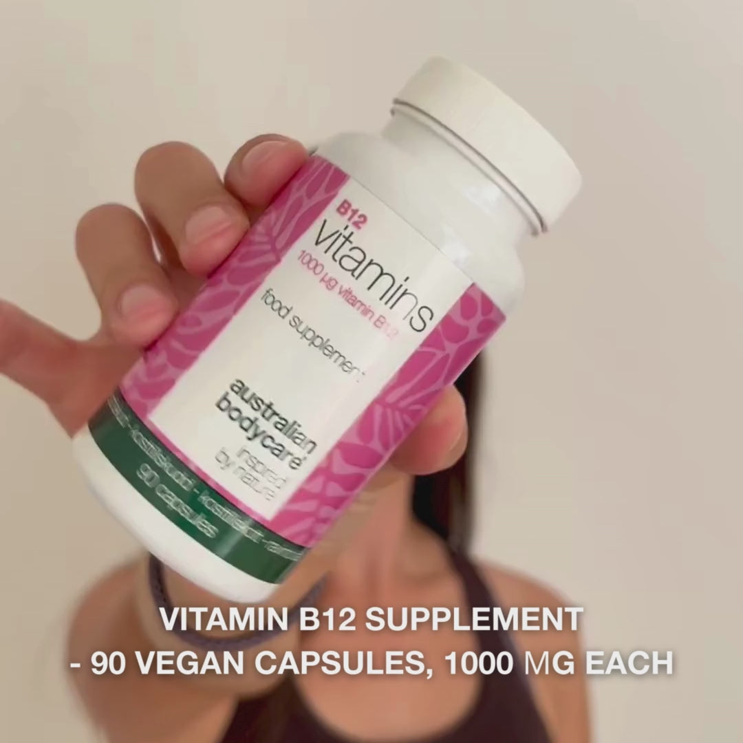 Close-up of a hand holding the Vitamin B12 dietary supplement bottle, opening the lid, and pouring out smooth, white capsules—showcasing the product for daily use to support energy, immune system, nervous system, and reduce tiredness.